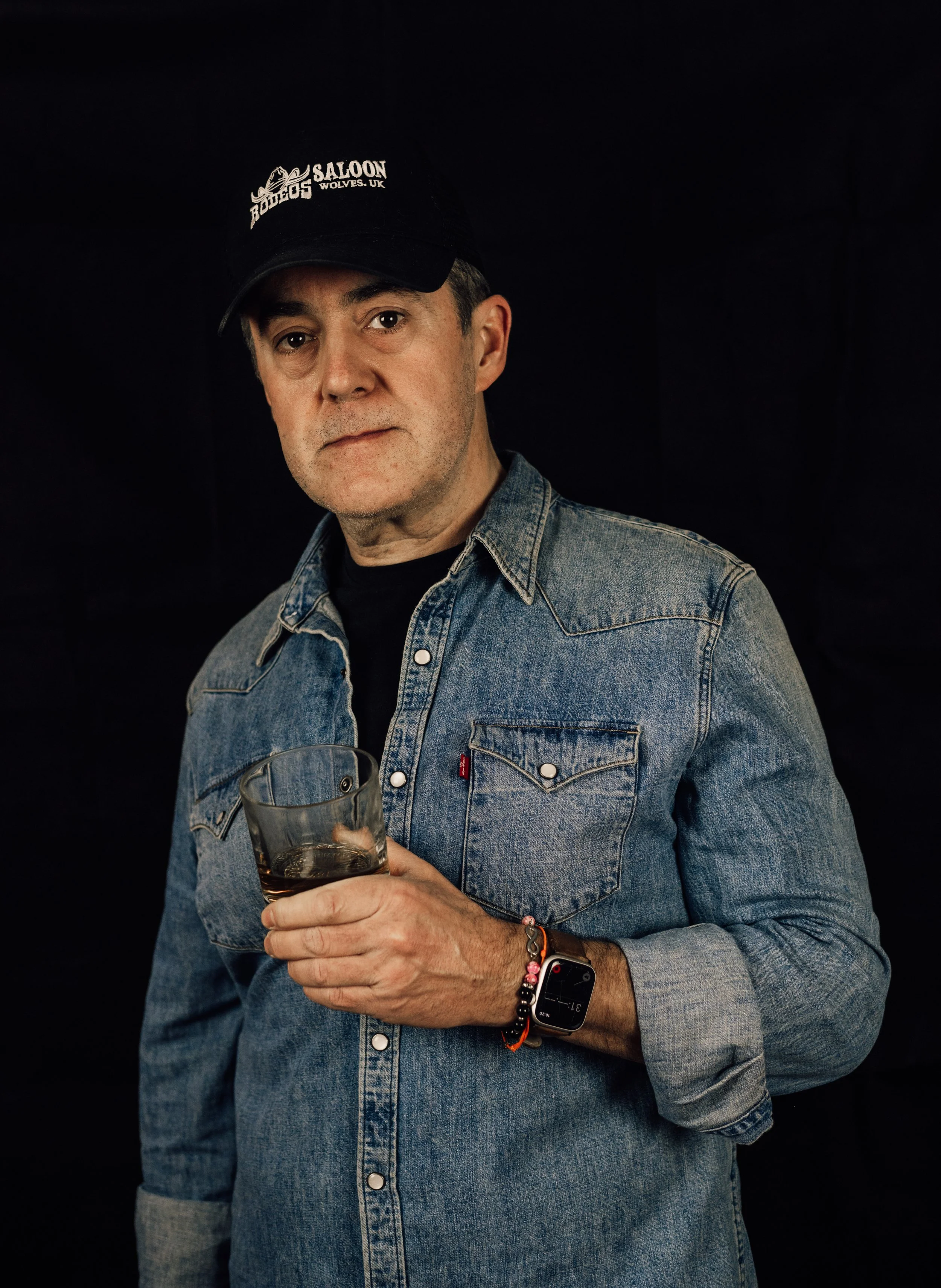 Dan Jones in a denim shirt and black cap, holding a glass